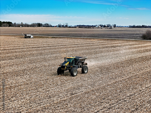 Self propelled spreader applying fertilizer to a field before tilling with farm scene in the distance