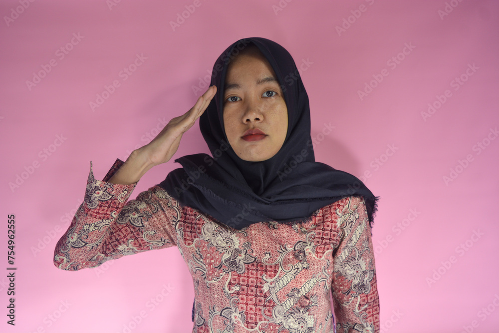 A young asian woman wearing hijab and wearing batik with a hand gesture of salute A young asian woman wearing hijab and wearing batik with a hand gesture of salute