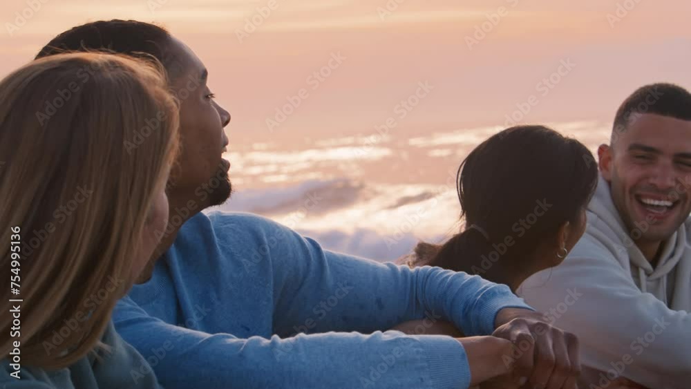 Close up shot of young couple with friends wearing casual clothing sitting relaxing on beach at dawn - shot in slow motion Close up shot of young couple with friends wearing casual clothing sitting relaxing on beach at dawn - shot in slow motion