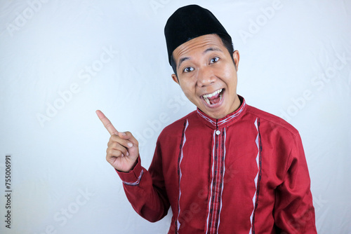 Smiling expression of muslim asian man, pointing finger an empty space. Advertising concept photo