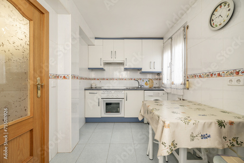 Dining table with oilcloth tablecloth with metal chairs in the kitchen of a house with white carpentry with blue details and light stoneware floors