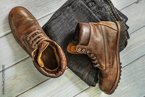 A pair of brown leather hiking boots with folded jeans on a light wooden surface