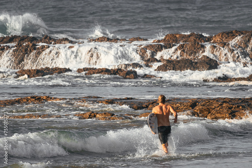 Shirtless surfer entering the ocean quickly with his surfboard held by his arm