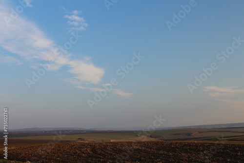 A landscape with a large field and blue sky with clouds