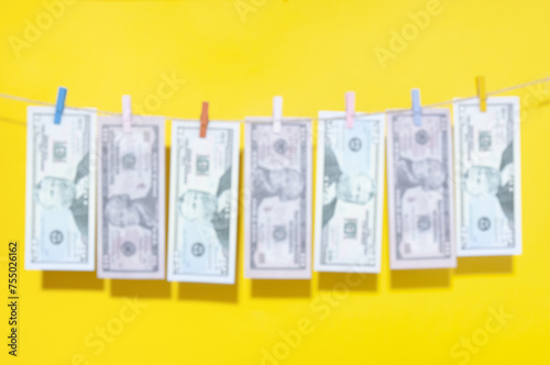 Blurring image of Dollar banknotes hanging on rope with  clothespins on yellow background