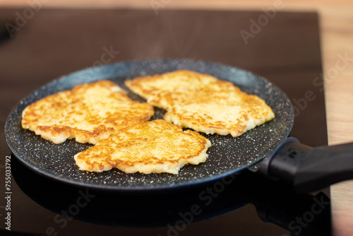 Golden-brown potato pancakes frying in a speckled non-stick pan on a hob.