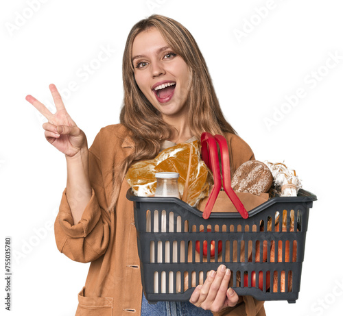 Blonde woman with basket of essentials in studio joyful and carefree showing a peace symbol with fingers.