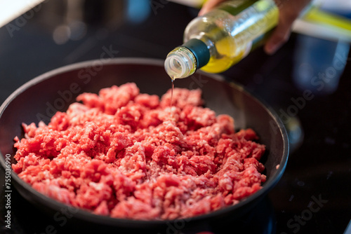 adding olive oil to mince meat in frying pan. photo
