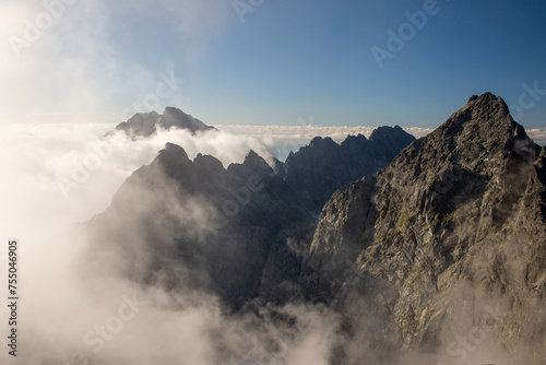 Panoramic view from Slovakia High Tatras Mountain peak Rysy in the foggy summer moring. Highest peak Gerlach covered by clouds in the bacground and fog in the foregroud with blue cloudless. sky photo