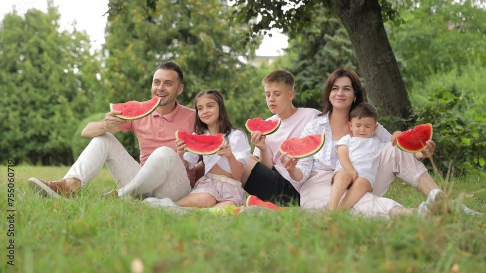 Happy family sharing watermelon on grass surrounded by trees in natural landscape. They enjoy spending time with each other