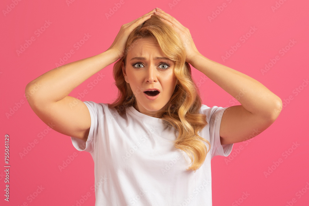 Desperate blonde woman touching head in frustration on pink background Desperate blonde woman touching head in frustration on pink background