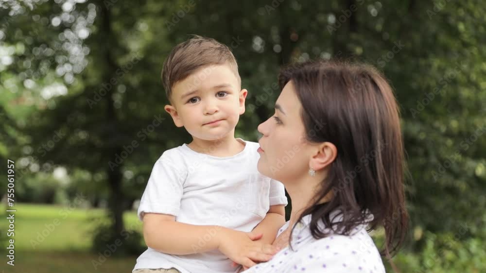 A woman is sharing a happy moment with a little boy in her arms, surrounded by trees and grass in a park. 