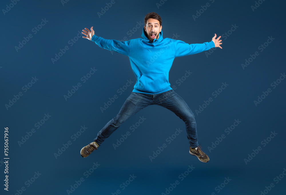 Crazy Offer. Funny Young Man Jumping Like A Star Over Blue Background
