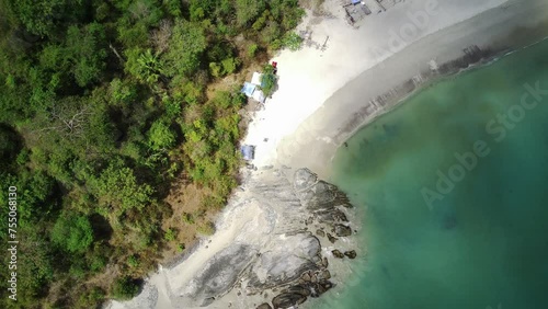 An aerial view of a secluded beach with powdery white sand, turquoise water, and a lush green forest lining the shore. photo