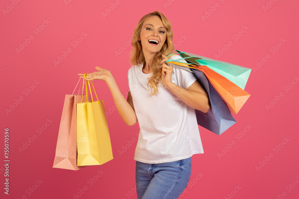 Beautiful European blonde lady carrying shopping bags on pink background