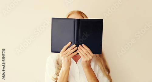 Young sad tired woman student covering her face with open book with blank cover