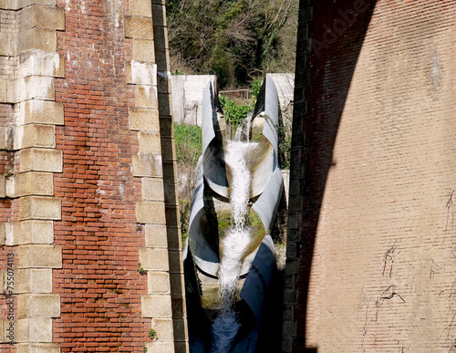 Rainwater drainage channel passing under the pylons of an old solid red brick railway bridge photo