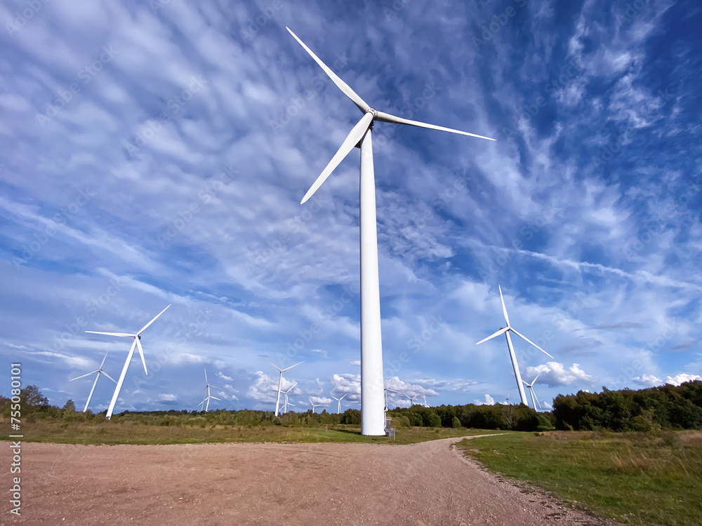 Fototapeta premium Windmill farm among fields and small trees. European Environment Initiative. Conservation of energy and fossil resources. Zero Ecological Footprint