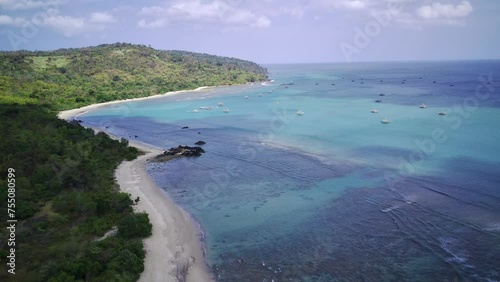 An aerial view of a secluded beach with powdery white sand, turquoise water, and a lush green forest lining the shore. photo