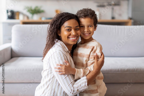 Cheerful black mother and her preteen son sharing loving embrace at home photo