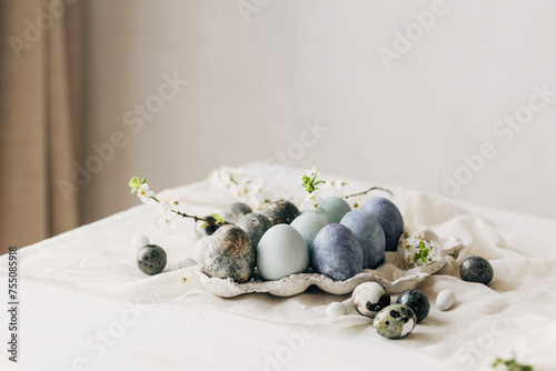 Stylish Easter eggs and spring flowers on rustic table. Happy Easter! Natural dye marble and blue eggs in tray and cherry blossoms. Happy Easter! Holiday minimal still life © sonyachny