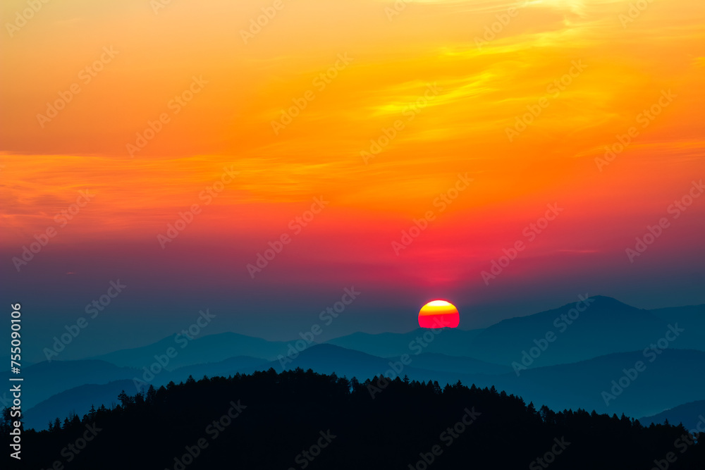The rising sun over the mountains, turning the sky red and yellow. In the foreground is the silhouette of the forest.