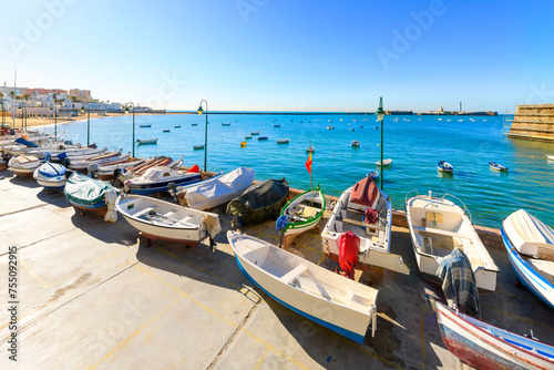 Fishing boats along the harbor and in the sea at La Caleta Beach in the historical center of the Andalusian city of Cádiz, Spain.