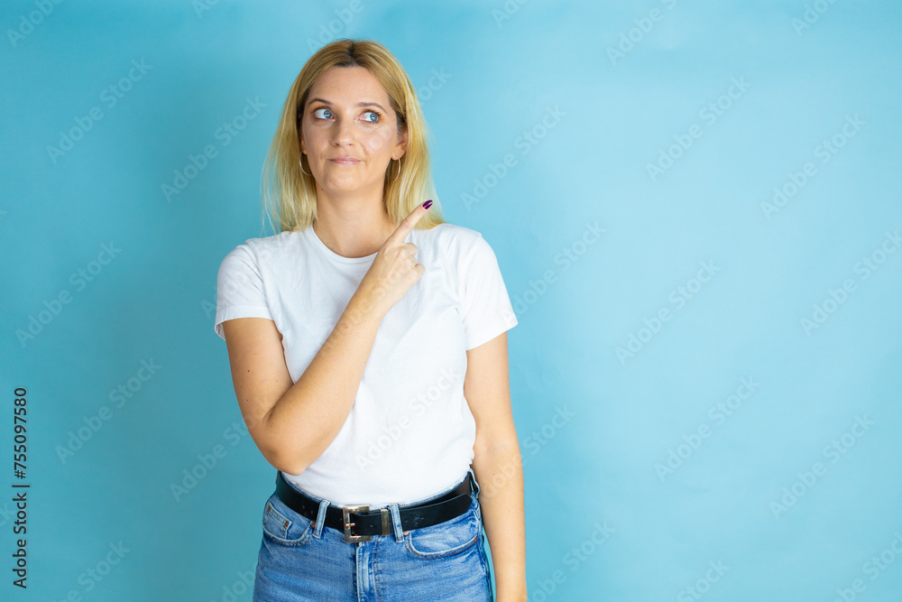 Young beautiful woman wearing casual t-shirt over isolated blue background confused and pointing with hand and finger to the side Young beautiful woman wearing casual t-shirt over isolated blue background confused and pointing with hand and finger to the side