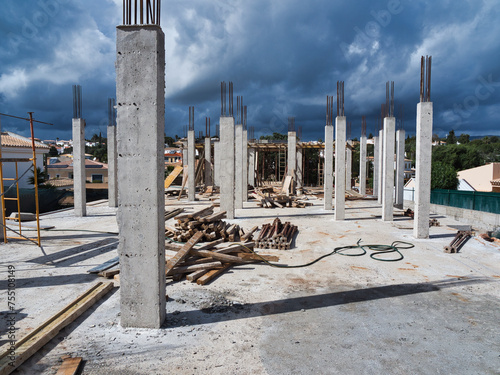 Construction Site: Building a New Home. Skeletal framework revealed in the form of numerous pillars, iron reinforcements, stacks of cement, wooden beams, and supporting structures.