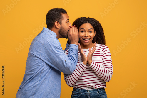 Cheerful Black Man Sharing Secrets With His Excited Girlfriend, Whispering To Ear