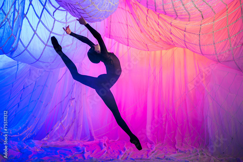 Ballerina dancer dances in a room with white curtains made of thin airy fabric, illuminated by blue and red spotlights.