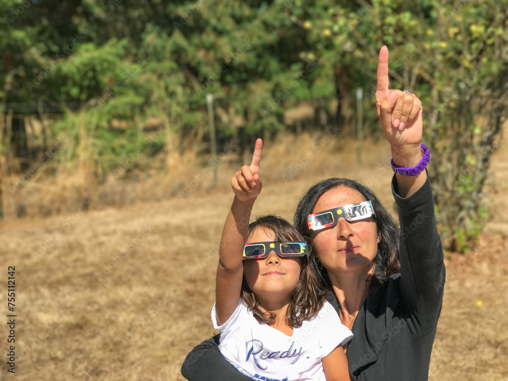 Mother and daughter, family viewing solar eclipse with special glasses in a park - obrazy, fototapety, plakaty 