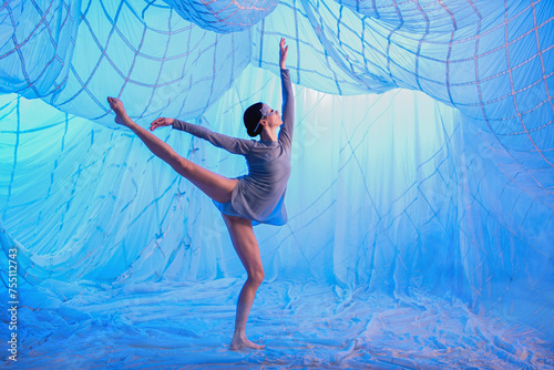 Ballerina dancer in a room with white drapes made of thin airy fabric, illuminated by blue spotlights. photo