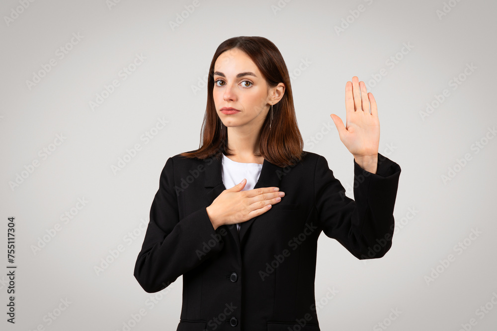 Solemn businesswoman in a black suit takes an oath with her right hand raised Solemn businesswoman in a black suit takes an oath with her right hand raised