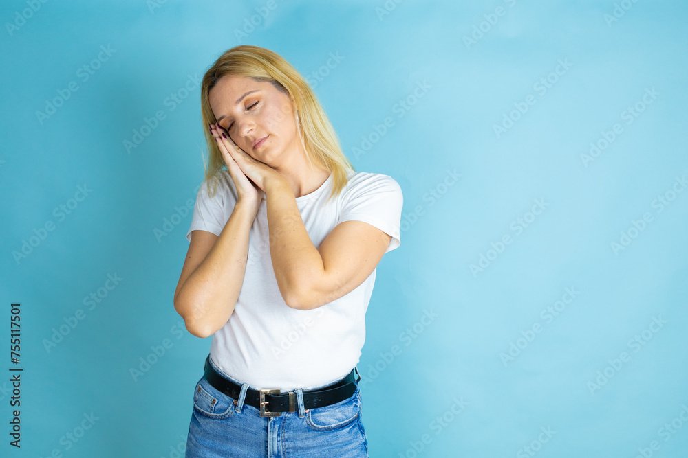 Young beautiful woman wearing casual t-shirt over isolated blue background sleeping tired dreaming and posing with hands together while smiling with closed eyes. Young beautiful woman wearing casual t-shirt over isolated blue background sleeping tired dreaming and posing with hands together while smiling with closed eyes.