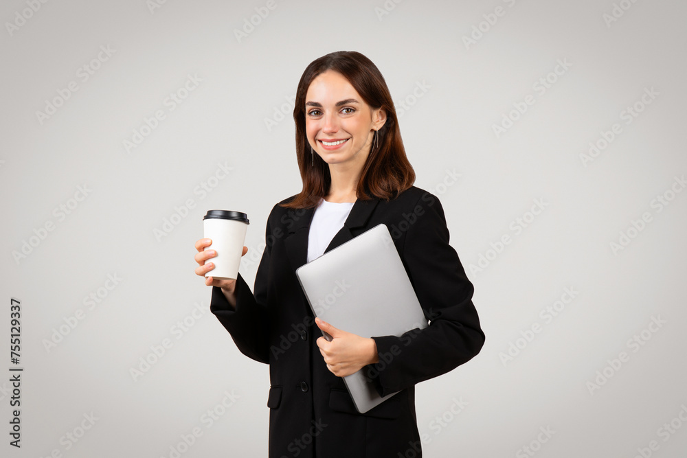 Smiling professional woman dressed in a black suit holding a takeaway coffee cup Smiling professional woman dressed in a black suit holding a takeaway coffee cup
