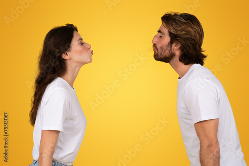 Side profile of a young man and woman in white t-shirts facing each other with puckered lips
