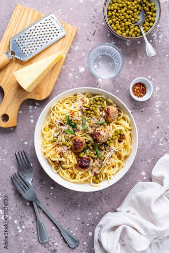 Spaghetti with meatballs and cream sauce is served on a plate with herbs and parmesan.