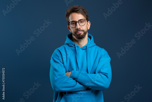 Man wearing glasses and blue hoodie looking disinterested, standing with arms crossed photo