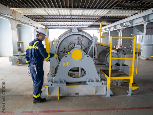 Seaman crew member of cargo vessel equipped with personal protective equipment is doing maintenance painting of mooring winch on aft station