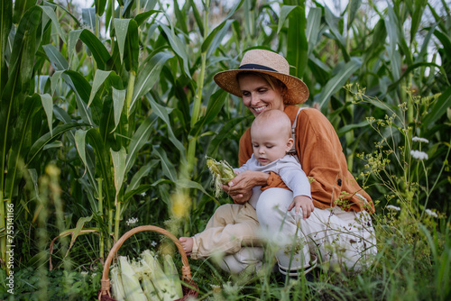 Portrait of female farmer with beautiful baby harvesting corn on the field.