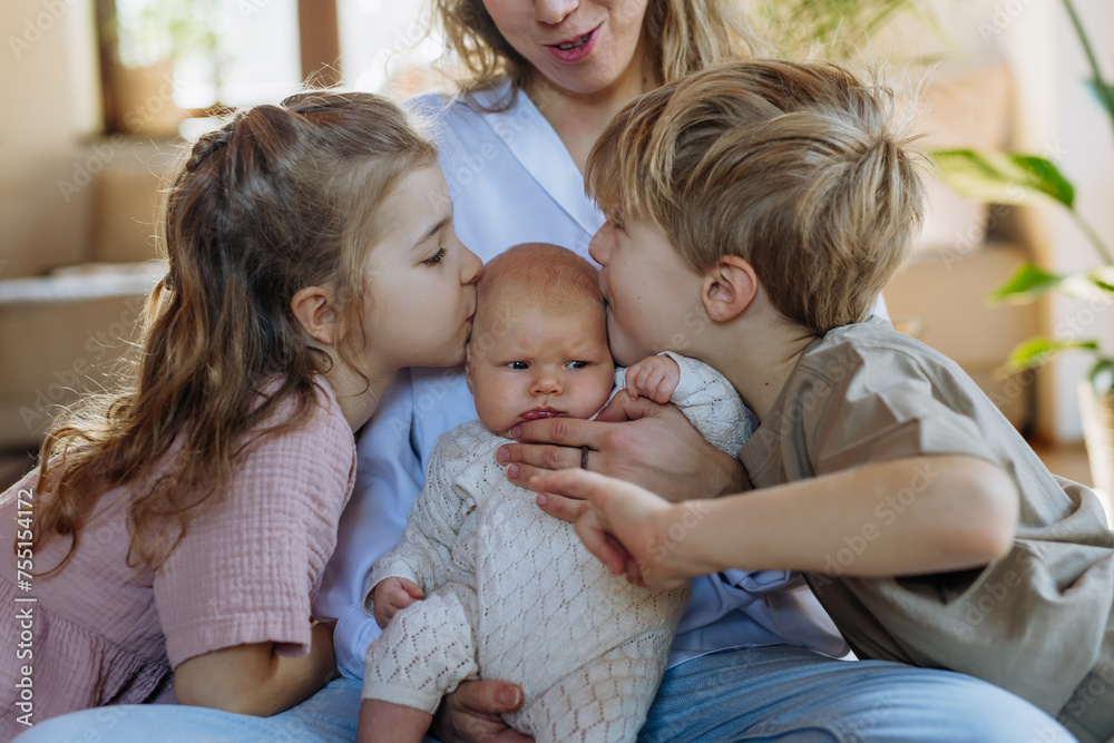 Siblings kissing the cheeks of a little baby. Big brother and big sister meeting newborn sister, enjoying together time. Siblings kissing the cheeks of a little baby. Big brother and big sister meeting newborn sister, enjoying together time.