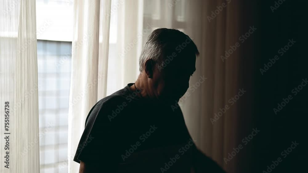 Depressed senior man stands by window in the shadows struggling with old age and mental illness. Pensive older 70s person feeling hopeless during challenging times Depressed senior man stands by window in the shadows struggling with old age and mental illness. Pensive older 70s person feeling hopeless during challenging times