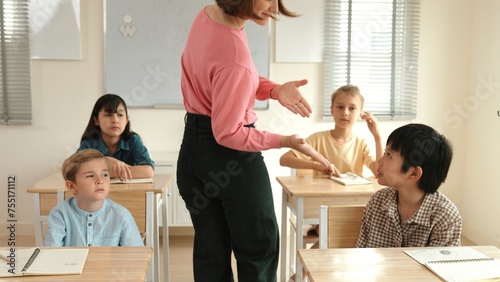 Caucasian teacher walking around classroom while explain classwork. Attraction instructor talking and explain lesson while diverse student listening ans working or taking a note. Education. Pedagogy.