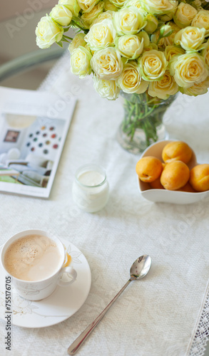 A cup of delicious morning coffee with organic yogurt, apricots and a bouquet of cream roses in the background. Selective soft focus
