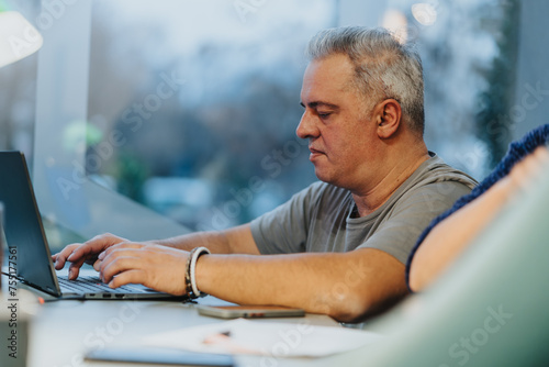 Mature man concentrating on work using laptop at home in evening.