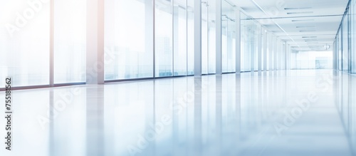 This image showcases a long hallway in a business office with numerous glass walls. The corridor is empty, with a white room visible in the background, creating a modern and spacious atmosphere.