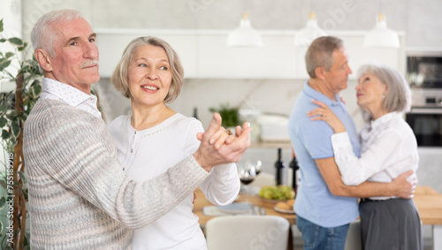 Couples of elderly women and men dancing in kitchen at home