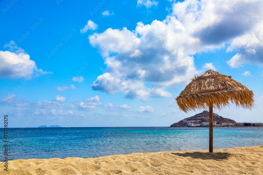 Umbrella on the sandy beach by the sea and cloudy sky. Vacation background. Idyllic beach landscape on Mykonos island, Greece Umbrella on the sandy beach by the sea and cloudy sky. Vacation background. Idyllic beach landscape on Mykonos island, Greece