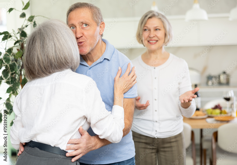 © JackF - In cozy home atmosphere, senior woman hug and kiss on cheek, say goodbye after party with elderly male friend, his female partner wife is in background